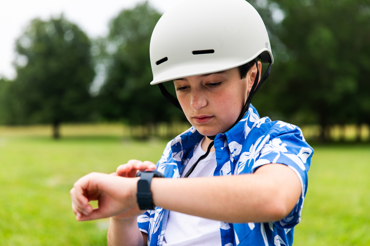 A child wearing a bike helmet outdoors checking his kids GPS smart watch.